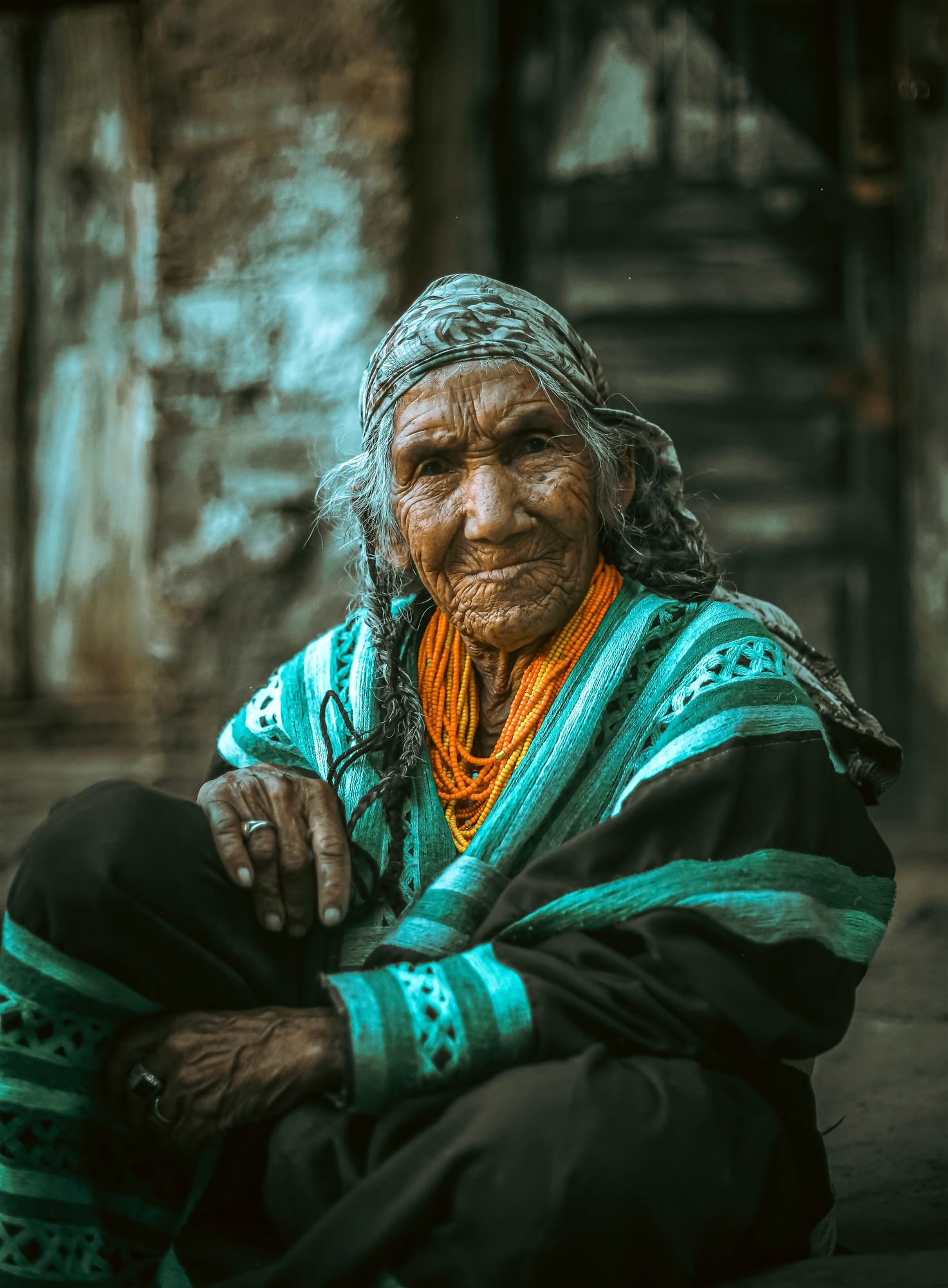 A Kalash elder in a traditional beaded headdress and woven shawl, seated in a wooden doorway